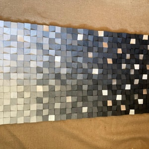 May include: A wall art piece made of wood blocks in shades of gray, transitioning from light to dark. The blocks are arranged in a grid pattern, creating a gradient effect.