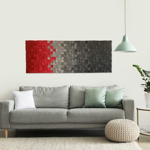 May include: A modern wall art piece made of wood with a red and gray geometric pattern. The art is hanging on a white wall above a gray sofa with pillows.