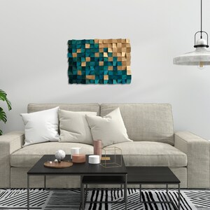 May include: A teal and gold geometric wall art piece hangs above a beige sofa with pillows. The sofa is in front of a white wall with a black and white patterned rug underneath.