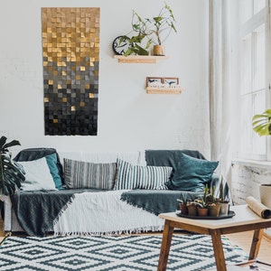 May include: A living room with a gray and gold geometric wall art piece, a gray couch with pillows, a coffee table with plants, and a large window with white blinds.