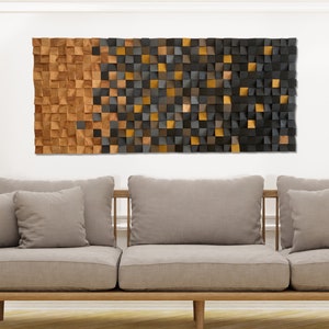 May include: A modern wall art piece made of wood with a geometric design. The piece is made up of small squares of wood in shades of brown, black, and gold. The piece is hanging on a white wall above a gray sofa.