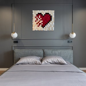 May include: A gray upholstered bed with a gray headboard and two pillows. A red and white heart-shaped wall art hangs above the bed.