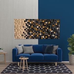 May include: A large, rectangular wooden wall art piece with a geometric design. The artwork features a gradient of colors, transitioning from light beige to black and gold. It hangs above a blue sofa in a modern living room setting.