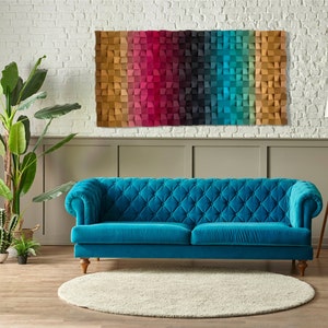 May include: A teal blue velvet sofa with tufted buttons sits in front of a white brick wall with a colorful geometric wall art piece above it. The sofa has a wooden frame and legs.