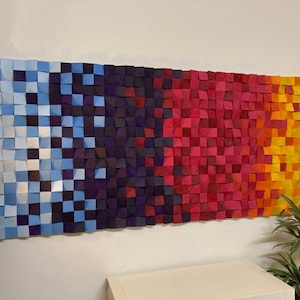 May include: A wall art piece made of wood squares in shades of blue, purple, red, orange, and yellow. The squares are arranged in a gradient pattern, creating a colorful and abstract design.