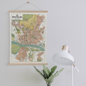 May include: A vintage map of Bratislava, Slovakia, printed on paper and framed with a wooden frame. The map shows the city's streets and landmarks, with a green and brown color scheme.