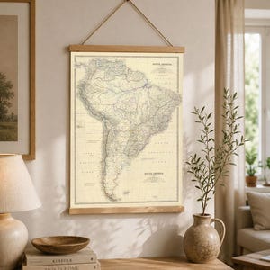 May include: A vintage-style wall map of South America printed on cream-colored paper, secured between two horizontal wooden slats at the top and bottom, and suspended by a thin brown rope attached to the top wooden bar.