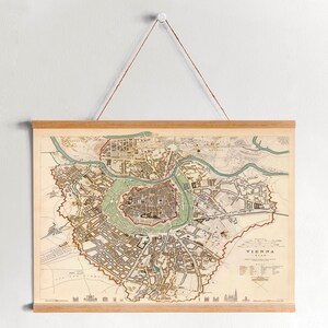 May include: A vintage map of Vienna, Austria, printed on paper and framed in wood. The map shows the city's streets and landmarks in detail, with a key to the different features.