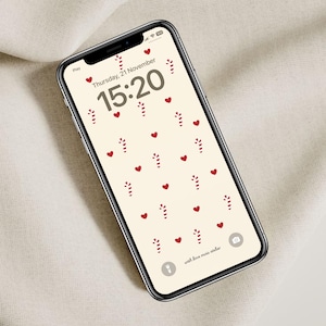 Puede incluir: Un teléfono inteligente que muestra un reloj digital con la hora 15:20, la fecha jueves 21 de noviembre y un patrón de fondo de corazones rojos y bastones de caramelo. El texto "with love, moira atelier" está en la parte inferior de la pantalla.