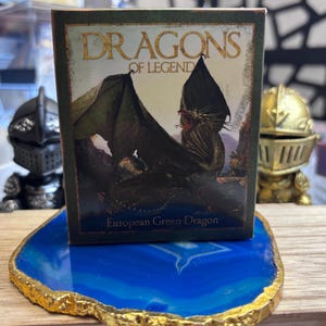 May include: A small box with the words "DRAGONS OF LEGEND" and an illustration of a green dragon. The box is on a blue and gold decorative coaster. The text "European Green Dragon" is at the bottom of the box.