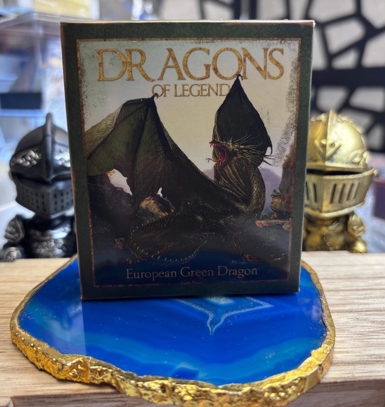 May include: A small box with the words "DRAGONS OF LEGEND" and an illustration of a green dragon. The box is on a blue and gold decorative coaster. The text "European Green Dragon" is at the bottom of the box.