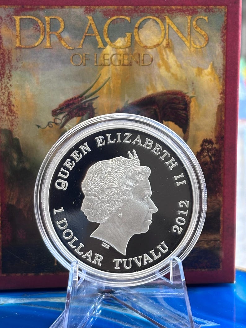 May include: A silver coin featuring Queen Elizabeth II, dated 2012, with the text "1 DOLLAR TUVALU." The coin is displayed in front of a box with the words "DRAGONS OF LEGEND" and a dragon illustration.
