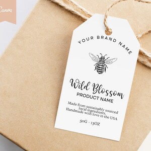 Puede incluir: Una etiqueta de regalo blanca con texto negro y una ilustración de una abeja. El texto dice "YOUR BRAND NAME", "Wild Blossom", "PRODUCT NAME", "Hecho con ingredientes locales de origen sostenible. Hecho a mano con amor en los Estados Unidos", y "50G - 1.3OZ".