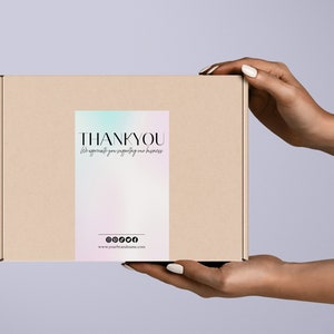 Pu&ograve; includere: Una scatola di cartone marrone con un adesivo di ringraziamento. L'adesivo ha uno sfondo olografico con un gradiente arcobaleno e il testo "THANK YOU for supporting my business".