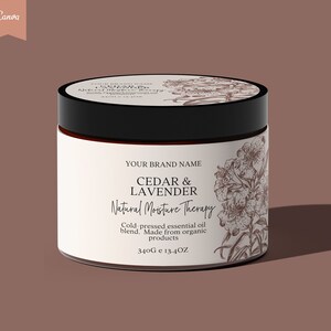 Op de afbeelding: Een witte pot met een zwarte deksel en een bruin etiket. Het etiket heeft een bloemmotief en de tekst "YOUR BRAND NAME CEDAR & LAVENDER Natural Moisture Therapy Cold-pressed essential oil blend. Made from organic products 340G e 13.4OZ".