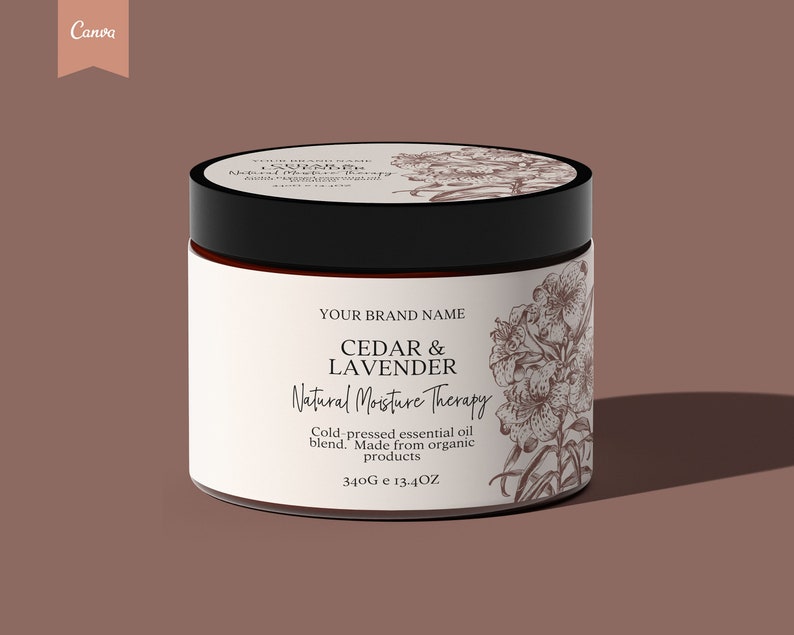 Op de afbeelding: Een witte pot met een zwarte deksel en een bruin etiket. Het etiket heeft een bloemmotief en de tekst "YOUR BRAND NAME CEDAR & LAVENDER Natural Moisture Therapy Cold-pressed essential oil blend. Made from organic products 340G e 13.4OZ".