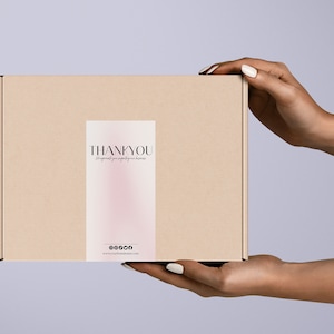 Pu&ograve; includere: Una scatola di cartone marrone con un adesivo rosa e bianco che dice "THANK YOU" e ha un indirizzo di sito web. La scatola &egrave; tenuta da due mani.