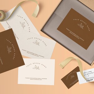 Pu&ograve; includere: Una collezione di biglietti da visita e una scatola con un'etichetta. I biglietti sono in tonalit&agrave; marrone e crema, con il testo "YOUR BRAND NAME" e un motivo floreale. &Egrave; presente anche un nastro.