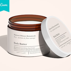 Op de afbeelding: Een witte pot met een bruin deksel gevuld met body butter. De pot is gelabeld met "Maison D'Houre Botanicals No.5 - parfum de fleur sauvage Body Butter" en "340G e 13.4OZ Handmade in the USA".