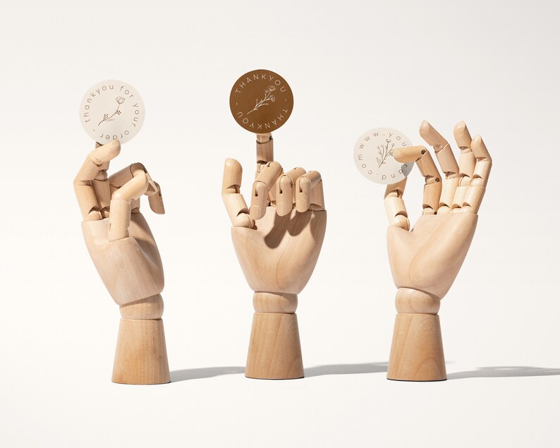 Pu&ograve; includere: Tre adesivi rotondi con disegni floreali e le parole "grazie per il tuo ordine" e "www.yourdomain.com" sono mostrati da mani di legno. Un adesivo &egrave; marrone e due sono bianco sporco.