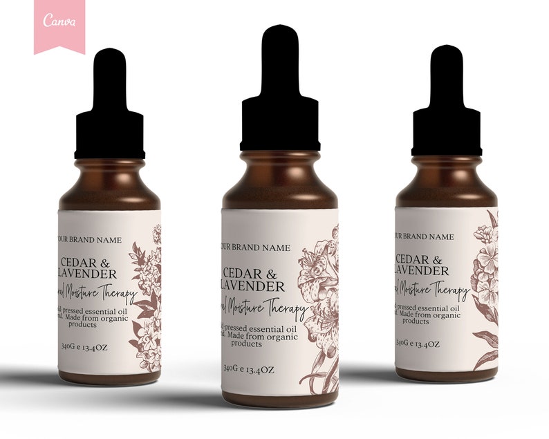 Op de afbeelding: Drie amberkleurige glazen flessen met druppelaars en witte etiketten. De etiketten bevatten een bloemenmotief en de tekst "Cedar & Lavender Essential Moisture Therapy", "geperste essenti&euml;le olie", "Gemaakt van biologische producten" en "340G e 13.4OZ".