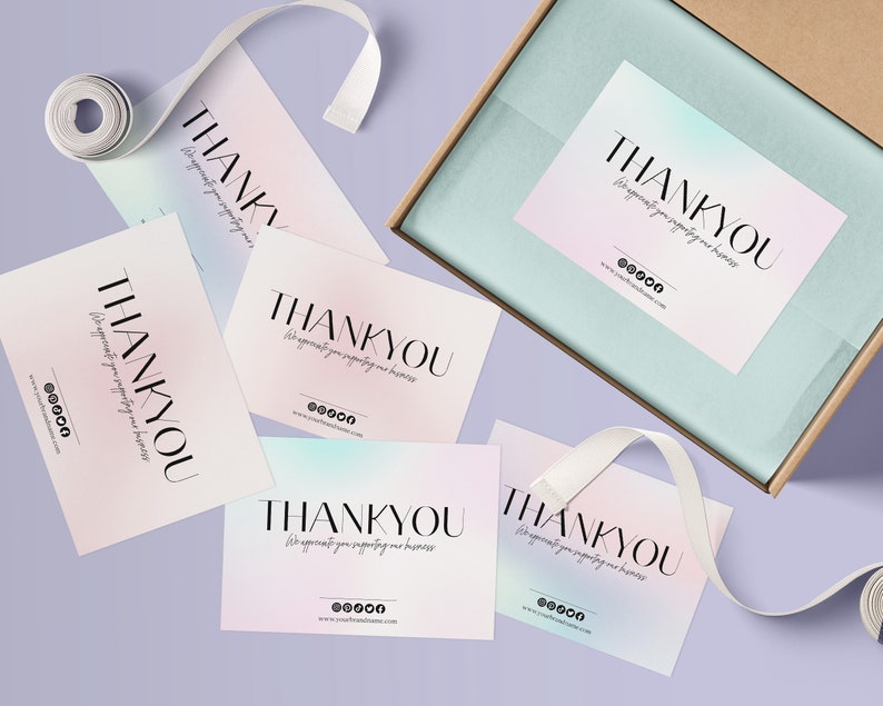 Pu&ograve; includere: Cinque biglietti di ringraziamento rosa pastello e blu con il testo "THANKYOU" in lettere nere. Il testo sottostante recita "We appreciate you supporting our business" con icone di social media e un indirizzo web. I biglietti sono su una superficie viola chiaro con un nastro bianco.