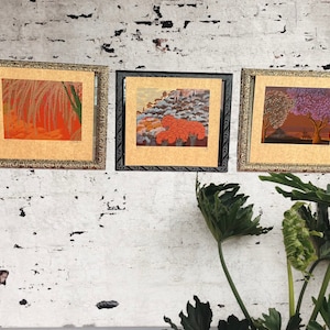 May include: Three framed pictures with gold trim and a white background. The pictures feature different landscapes with orange, purple, and green colors.