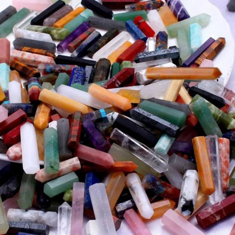 May include: A collection of colorful gemstone crystals in various shapes and sizes. The crystals are in shades of red, pink, purple, green, orange, and clear. Some crystals are hexagonal, while others are rectangular.