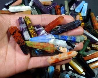 May include: A collection of colorful, pointed crystal wands in various shades of red, orange, yellow, green, blue, purple, and black. The wands are arranged in a hand, showcasing their unique patterns and textures.