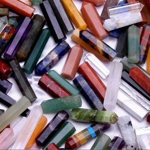 May include: A collection of various gemstone crystals in a variety of colors, including red, purple, green, and clear. The crystals are hexagonal in shape and appear to be polished. The crystals are scattered, creating a visually appealing display.