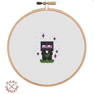 May include: Cross-stitch embroidery of a pixelated Enderman character from Minecraft. The design features a black body, purple eyes, and a green leaf-like shape on a green base, surrounded by purple star accents. The embroidery is set in a wooden hoop.