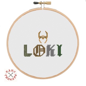 May include: A white embroidery hoop with a cross-stitch design of the word "LOKI" in different colors. The "O" is a circle with a stylized "A" inside. Above the word is a gold and yellow stylized horned helmet.
