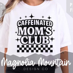 Puede incluir: Camiseta blanca con el texto "CAFFEINATED MOM'S CLUB" en negro. El diseño incluye estrellas y un patrón de tablero de ajedrez. La marca "Magnolia Mountain Design Co" se muestra debajo.