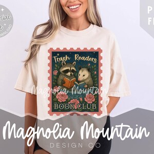 Könnte beinhalten: Cremefarbenes T-Shirt mit einem stempelartigen Design, das einen Waschbären und einen Opossum beim Lesen von Büchern zeigt, mit dem Text "Trash Readers Book Club". Das Shirt hat auch den Text "Magnolia Mountain Design Co."