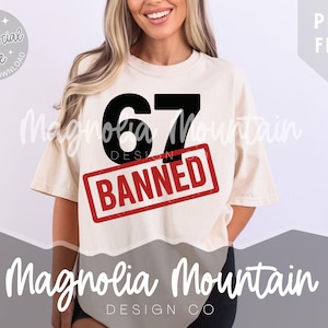 May include: Cream-colored t-shirt with the number "67" in black and the word "BANNED" in a red rectangle. The shirt also features the text "Magnolia Mountain DESIGN CO" in white.