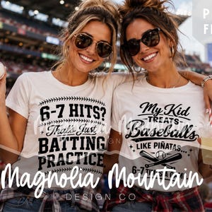 Op de afbeelding: Twee vrouwen dragen witte T-shirts met honkbalthema-afbeeldingen en zonnebrillen en poseren bij een honkbalwedstrijd. Op één shirt staat "6-7 HITS? That's Just BATTING PRACTICE", op het andere "My Kid TREATS Baseballs LIKE PIÑATAS". Het logo van Magnolia Mountain Design Co. is zichtbaar.