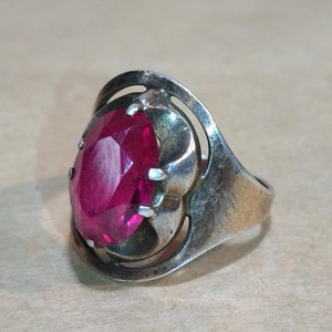 May include: A silver ring with a large, faceted, oval-shaped, pink gemstone set in a decorative, open-work setting.
