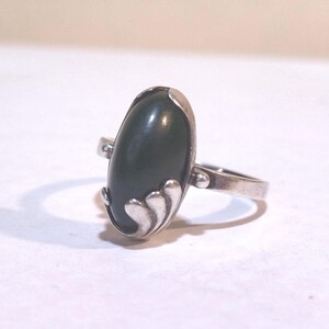 May include: A silver ring with a dark green oval gemstone set in a floral design.