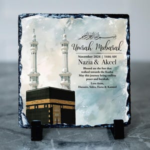 May include: A slate plaque with a watercolour painting of the Kaaba in Mecca, Saudi Arabia. The plaque has the text "Umrah Mubarak" and "November 2024 | 1446 AH Nazia & Akeel Blessed are the feet that walked towards the Kaaba. May this journey being endless peace and barakah. Love from, Hussain, Sidra, Foria & Kameel".