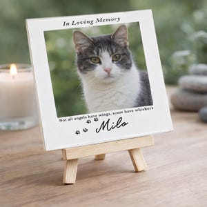 May include: A white ceramic tile featuring a framed photograph of a grey and white cat, presented on a miniature wooden easel. The tile is inscribed with "In Loving Memory", a quote, paw prints, and the name "Milo."
