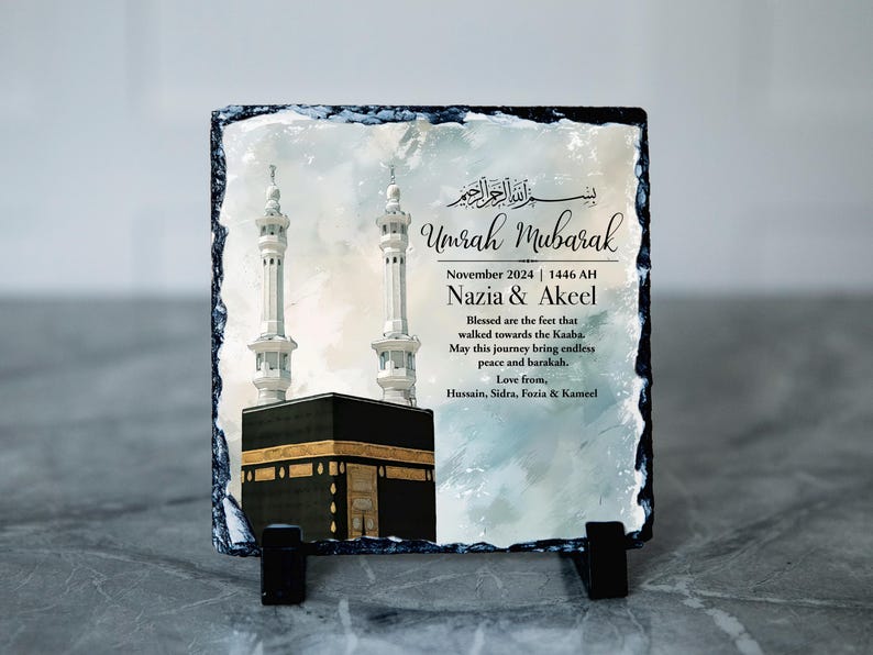 May include: A slate plaque with a watercolour painting of the Kaaba in Mecca, Saudi Arabia. The plaque has the text "Umrah Mubarak" and "November 2024 | 1446 AH Nazia & Akeel Blessed are the feet that walked towards the Kaaba. May this journey being endless peace and barakah. Love from, Hussain, Sidra, Foria & Kameel".