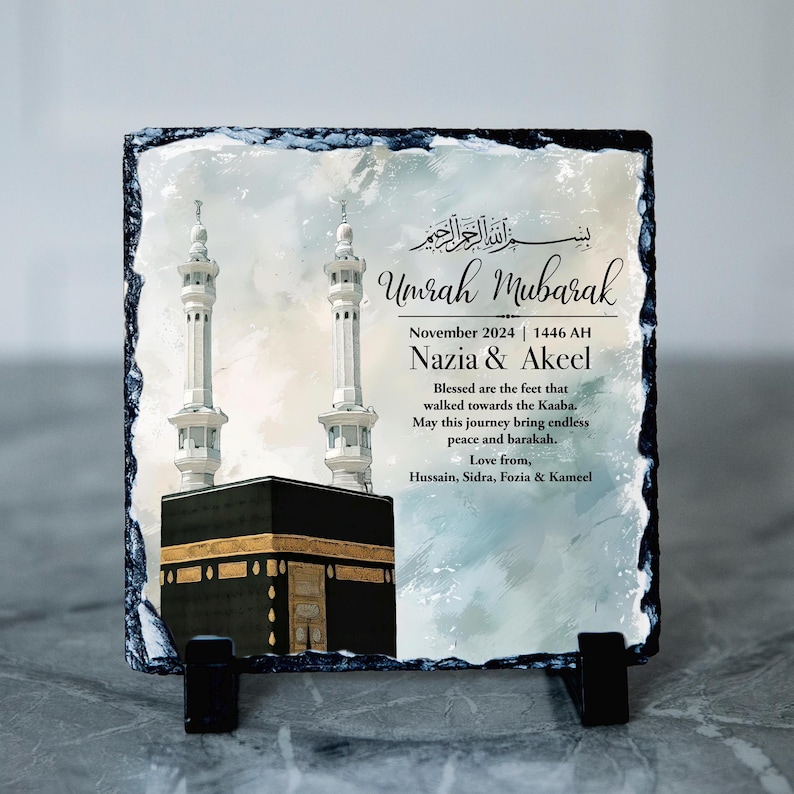 May include: A square slate plaque with rough, chipped edges featuring a printed image of the Kaaba and two minarets. The text reads: Umrah Mubarak, November 2024 | 1446 AH, Nazia & Akeel, and a blessing message from Hussain, Sidra, Fozia & Kameel.