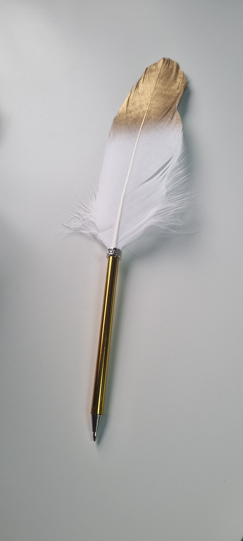 May include: A gold and white feather pen with a silver band. The pen is on a white background.