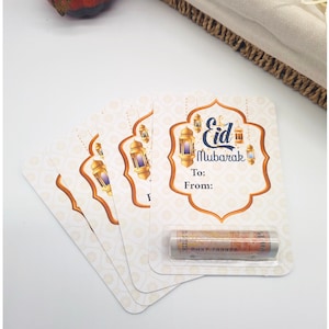 May include: Five white gift tags with a gold and orange border and a design of lanterns and the text "Eid Mubarak". The tags have blank spaces for "To:" and "From:". A rolled-up banknote is in a clear plastic sleeve on the top tag.