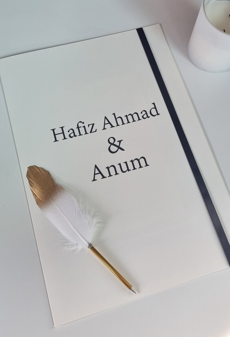 May include: A white card with black text that reads "Hafiz Ahmad & Anum". A gold and white feather pen is lying on the card.