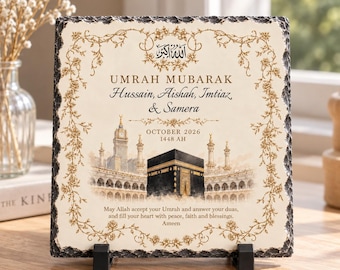 May include: A square slate plaque with rough edges featuring a gold floral border, an illustration of the Kaaba, and text reading Umrah Mubarak, Hussain, Aishah, Imtiaz & Samera, October 2026, 1448 AH, and a prayer for peace, faith, and blessings.