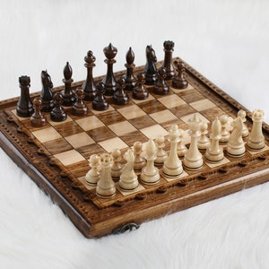 May include: A wooden chessboard with a carved border and a set of black and white chess pieces. The board is made of light and dark wood and has a traditional design.