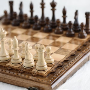 May include: A wooden chessboard with a brown and beige checkered pattern. The board has a carved wooden frame with a decorative design. White chess pieces are arranged on the board, with black pieces in the background.