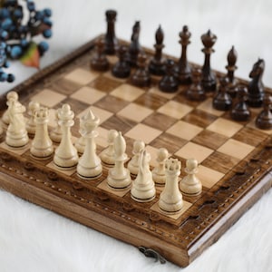 May include: A wooden chessboard with a carved border and a set of wooden chess pieces. The chessboard is open and the pieces are arranged in their starting positions.