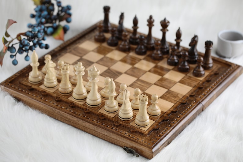 May include: A wooden chessboard with a carved border and a set of wooden chess pieces. The chessboard is open and the pieces are arranged in their starting positions.
